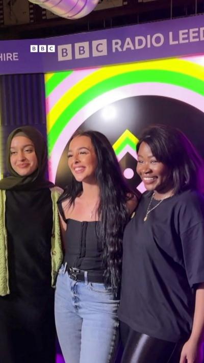 A woman wearing a headscarf on the left of a group of three, all smiling.