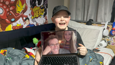 Riley smiles and holds a laptop screen with Ryan Reynolds and Blake Lively on it.