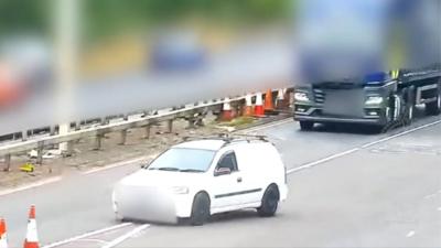 A small white van reverses back past a slip road exit, almost into a HGV