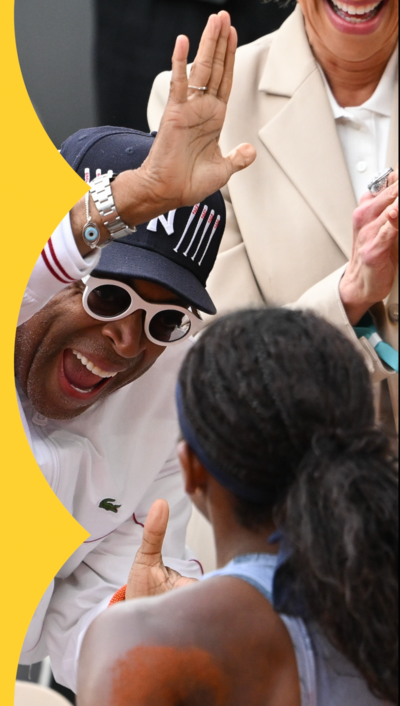 American film director Spike Lee, wearing  black hat and white sunglasses, holds up his hand.