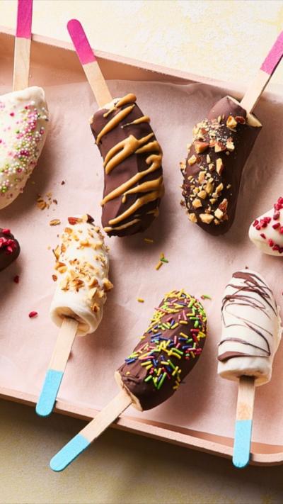 Eight lollies covered in sprinkles and chocolate on a pink tray. Some are not fully in frame.