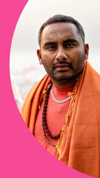 Amol Rajan looks at the camera, he is wearing an orange shawl and beads