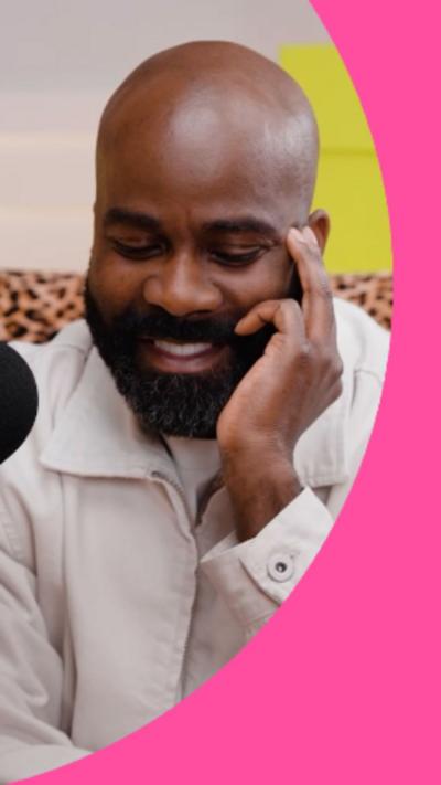 Melvin Odoom has a dark beard and is wearing a cream jacket. He's looking down and smiling.