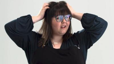 Woman with glasses holds her head and looks at the camera