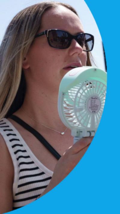 A woman cools her face with a hand-held electric fan