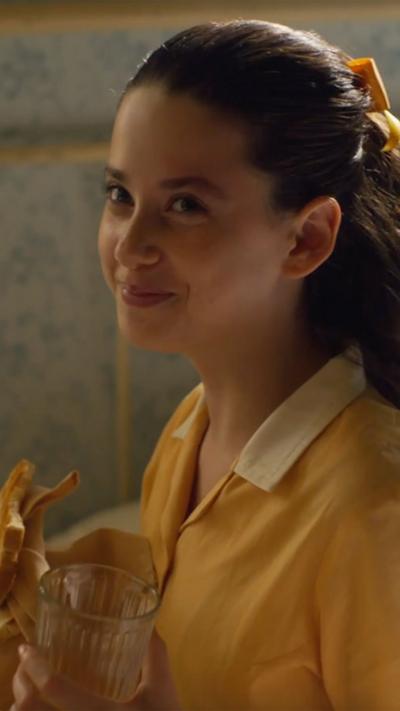 A young girl smiles, Josephine, she is wearing the malory towers bright yellow uniform.