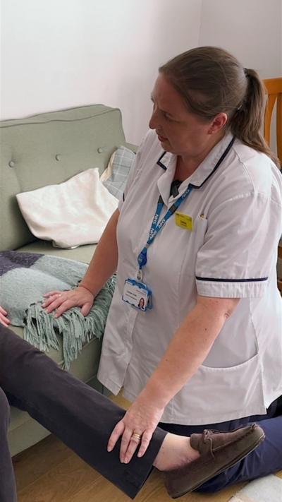 Woman in nurses uniform with dark hair holding a woman's leg in a room wiht a bed