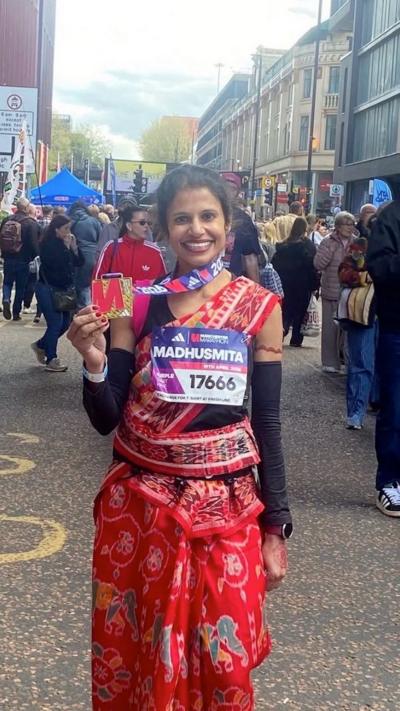 A woman dressed in a red Sari holding a Manchester Marathon medal