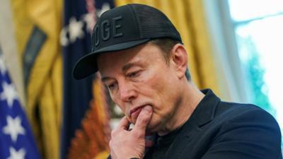 Elon Musk looks pensive while standing in the Oval Office