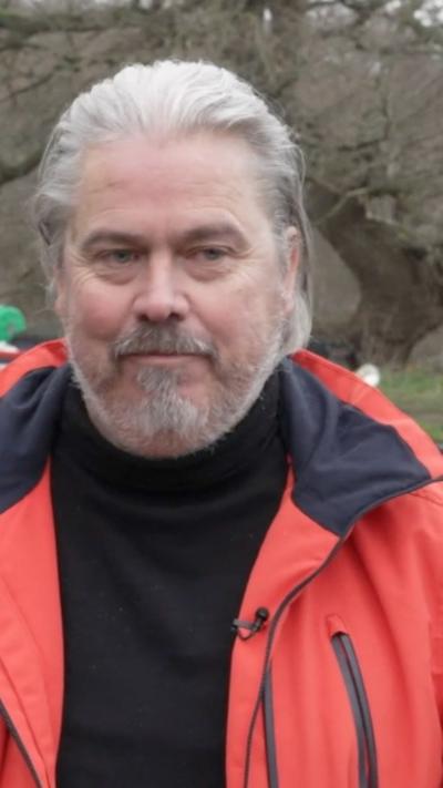 man with grey hair and beard in orange jacket