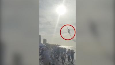 Jet flying above a crowd on a beach with a red circle around it.