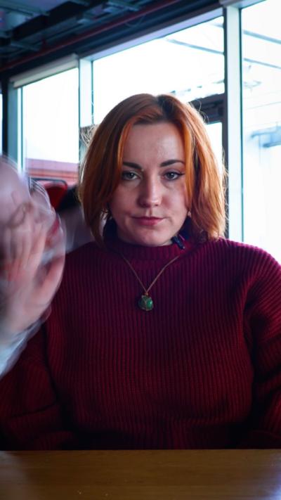 A woman frowns at the camera while a figure in a vampire cloak and makeup looms over her shoulder and into her face.