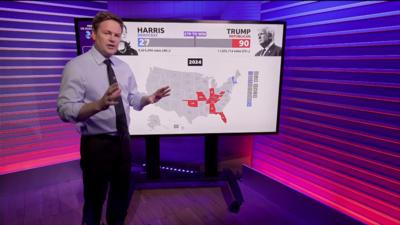 Christian Fraser standing and to his right, a touchscreen with a US map showing possible election results