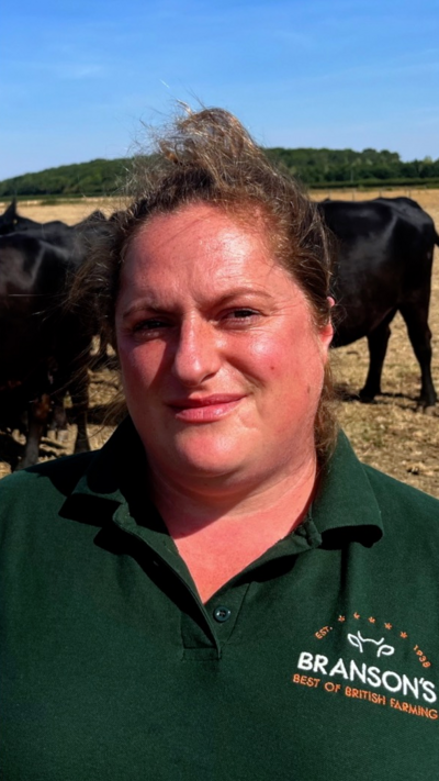 Female cattle farmer stands in front of cows, she is wearing a green polo shirt