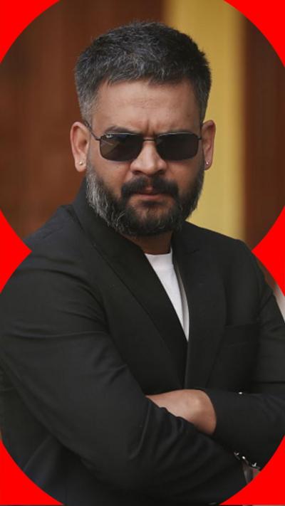 Man wearing black shades and a black blazer folds his arms.