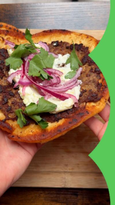 Smashed lamb flatbread on a wooden chopping board being lifted up 