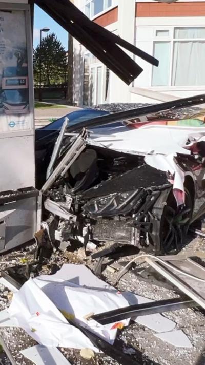 A black sports car crashed into a shattered bus shelter, with glass debris scattered around and a damaged structure visible.