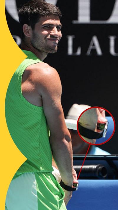 Carlos Alcaraz in green adjusts a wearable device at the Australia Open