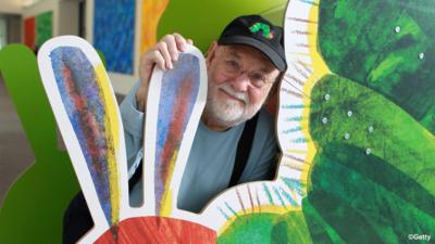 Eric Carle stands with a cardboard cut-out of the very hungry caterpillar