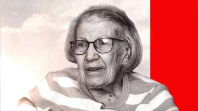 An elderly woman in a striped jumper and glasses looks into the distance