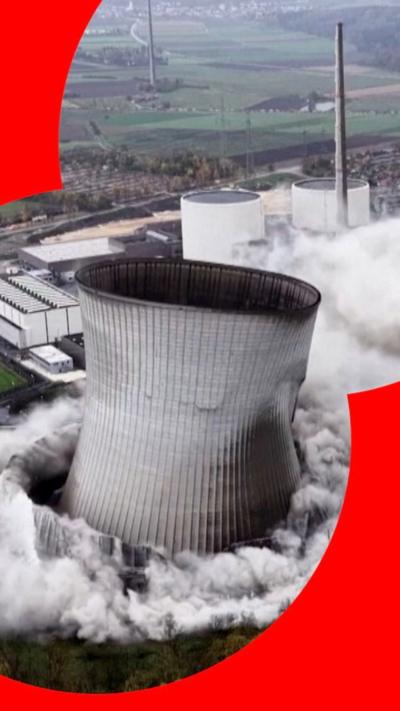 A grey concrete tower, mid-demolition, with plumes of white smoke at the bottom.