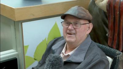 A Newcastle man wearing a flat cap and glasses, proudly and happily telling how he uses the local slang.