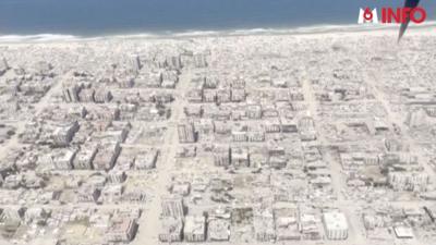 Bombed out buildings and rubble in Gaza, viewed from above, with the coastline visible at the top of the image.
