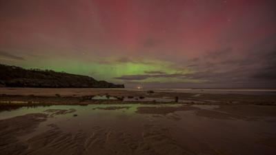 Red and green Northern Lights display above a dark beach