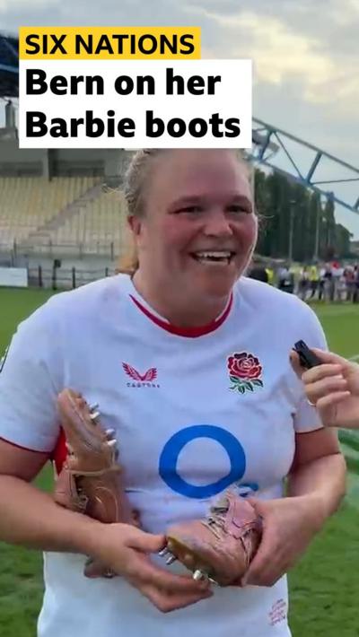 Sara Bern smiling and holding her pink rugby boots 