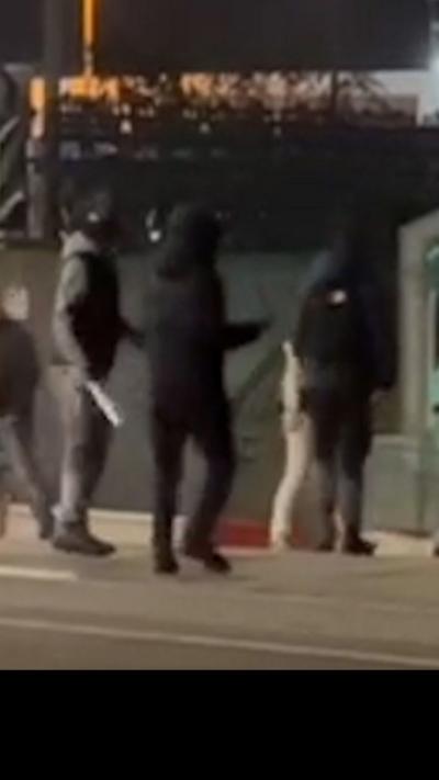 Three masked figures on a busy street, with a knife glinting in one of their hands.
