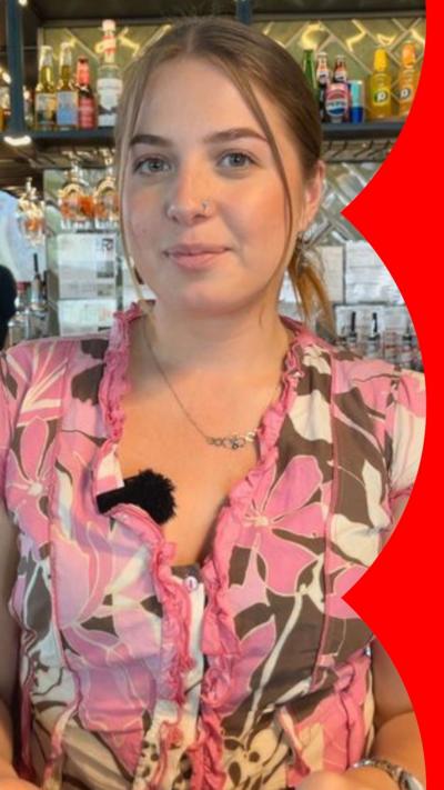 A woman with light brown hair stands in front of a bar