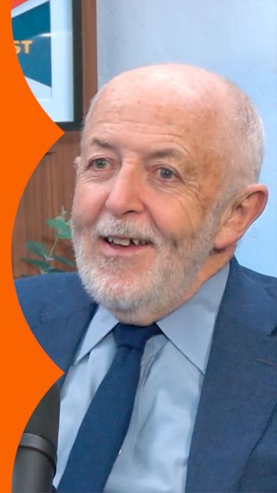 A man, Jeremy Bowen, in a blue suit and tie sits in front of a microphone