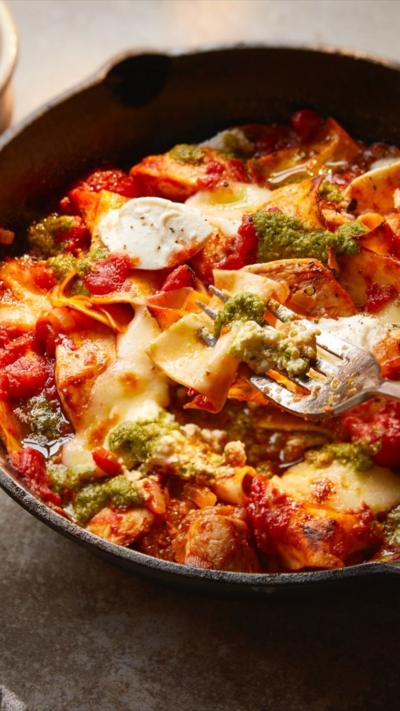 A one handled pan with chicken lasagne in. A hand holding a fork can also be seen. 