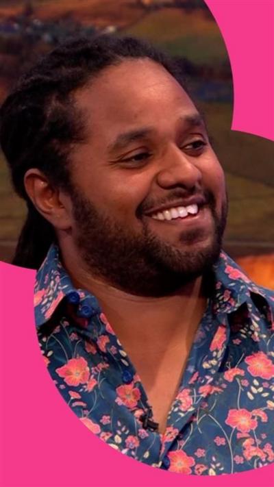 Hamza Yassin, in a blue shirt with red flowers, smiles in The One Show studio.