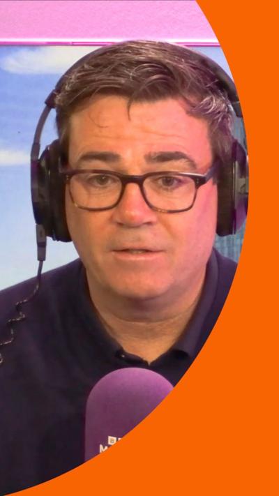 Andy Burnham in a dark shirt and glasses, sat at a Radio Manchester microphone