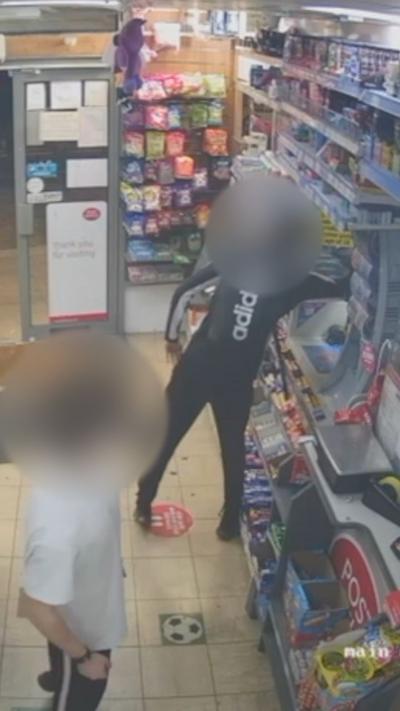 A CCTV image of two young people in an off licence with their faces blurred. One of them is reaching behind the counter.