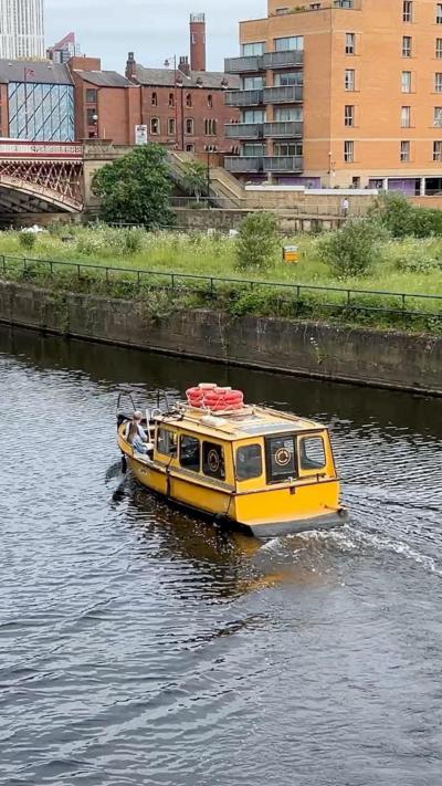A yellow water taxi on a river. In the background is various buildings including a block of flats with balconies