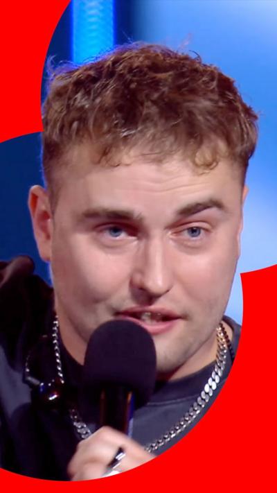 Singer Sam Fender holding mic and wearing silver necklace