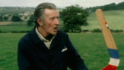 Man wearing shirt and jacket holds boomerang in a field