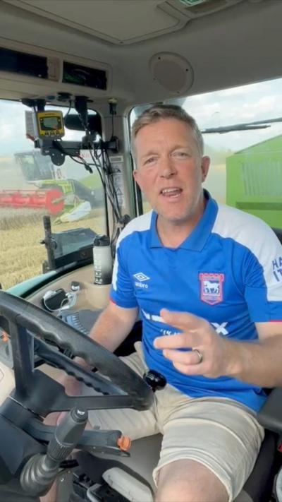 A man in a blue Ipswich Town shirt, sitting in a tractor, addresses the camera