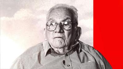 An elderly man wears glasses and a checked shirt