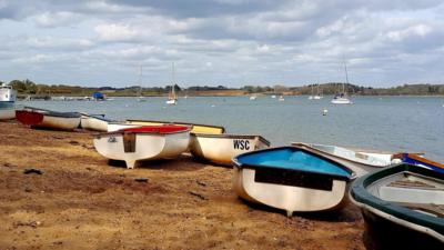 Sailing boats resting on a sandy beach with sailing area with more boats on in the distance 
