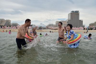 North Koreans splash in the water by the beach lined with hotels on an overcast day