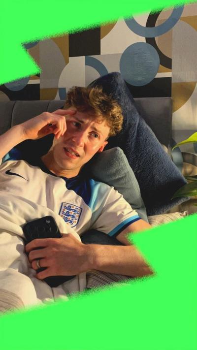 Reporter Jamie looking conflicted, wearing an England shirt, lying in bed and holding his phone.