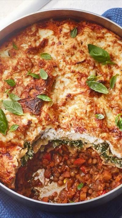 Aerial view of a large round dish with a lasagne in it and bay leaves on top. A spoonful has been taken away