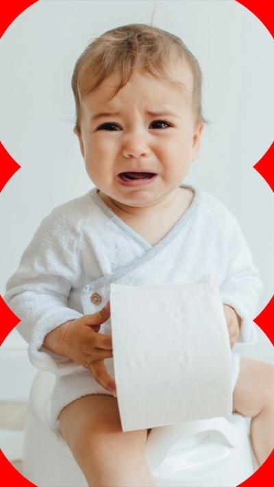 A child cries while holding a roll of toilet paper while sitting on a potty.