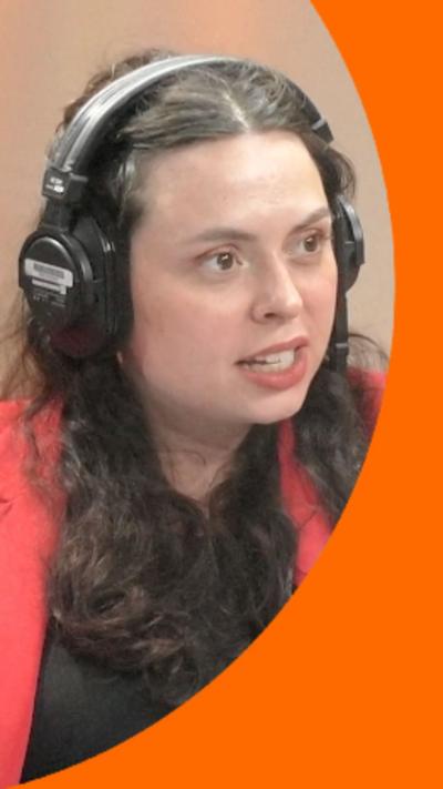 A woman with long, dark curly hair talks to someone off-camera