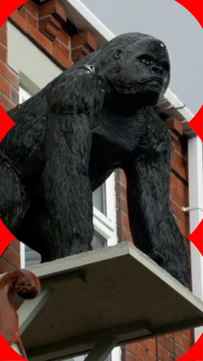 A gorilla statue mounted on a platform attached to the front of redbrick house.