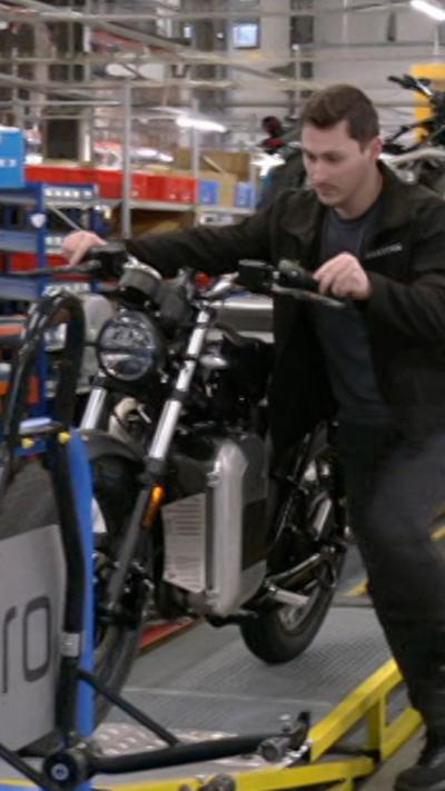 A man in a black jacket pushing a black motorcycle up a ramp in a factory