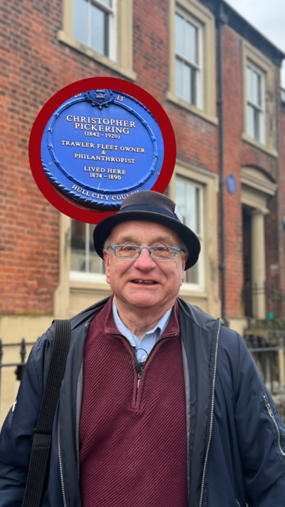 Paul Schofield standing on Coltman Street in Hull. He is wearing a blue coat unzipped, with a burgundy quarter-zip jumper underneath and a dark blue trilby hat.
